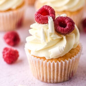 Image showing a decorated cupcake on a kitchen counter with fresh raspberries in the background.