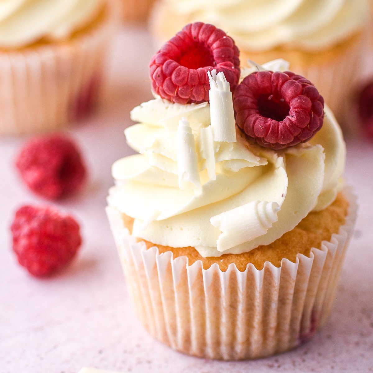 Image showing a decorated cupcake on a kitchen counter with fresh raspberries in the background.