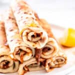 South African Pancakes with Cinnamon Sugar shown stacked on a plate with honey being drizzled over them.