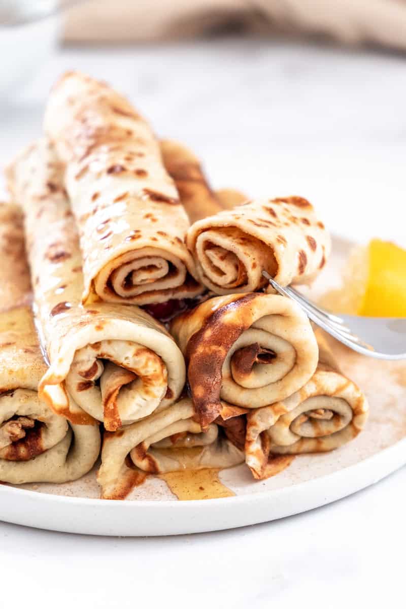 South African Pancakes with Cinnamon Sugar shown rolled up and stacked on a plate.