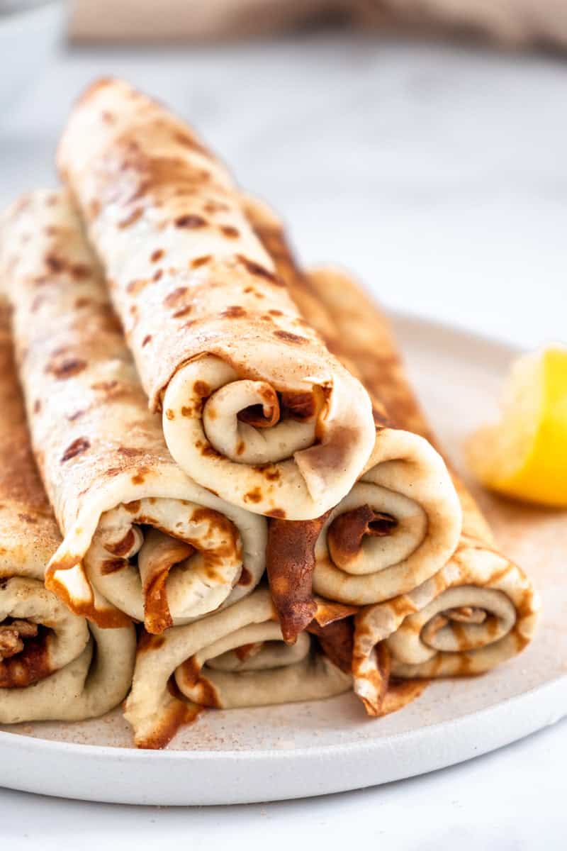 South African Pancakes with Cinnamon Sugar shown stacked on a plate next to a halved lemon. 