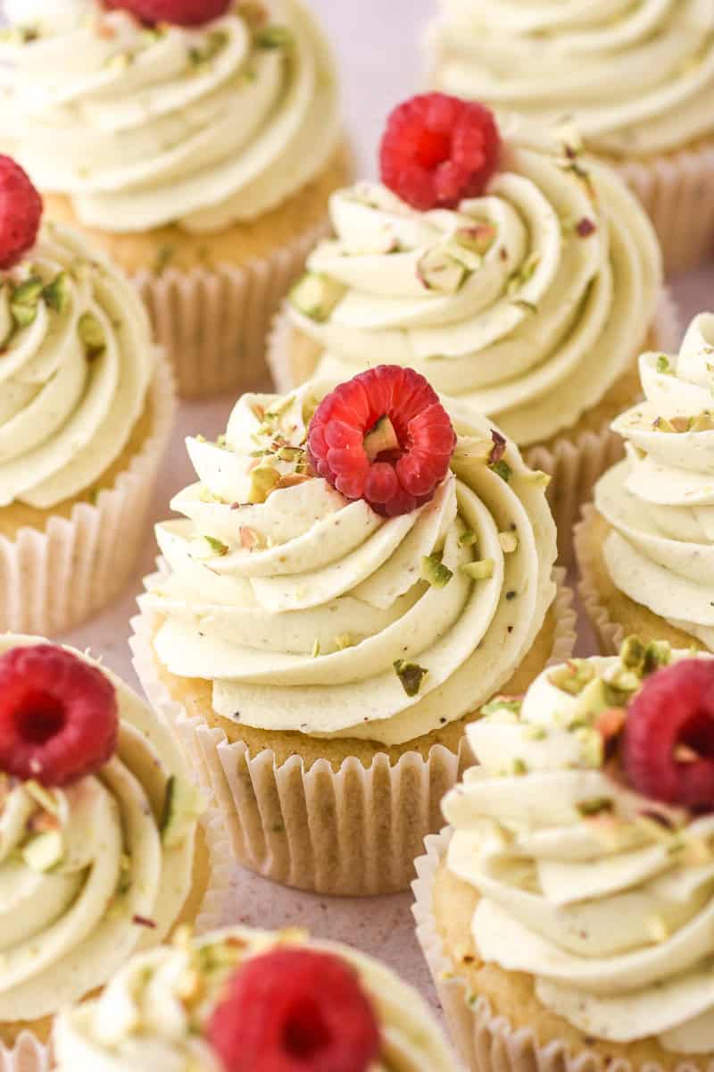 Pistachio Buttercream shown swirled onto cupcakes and decorated with raspberries. 