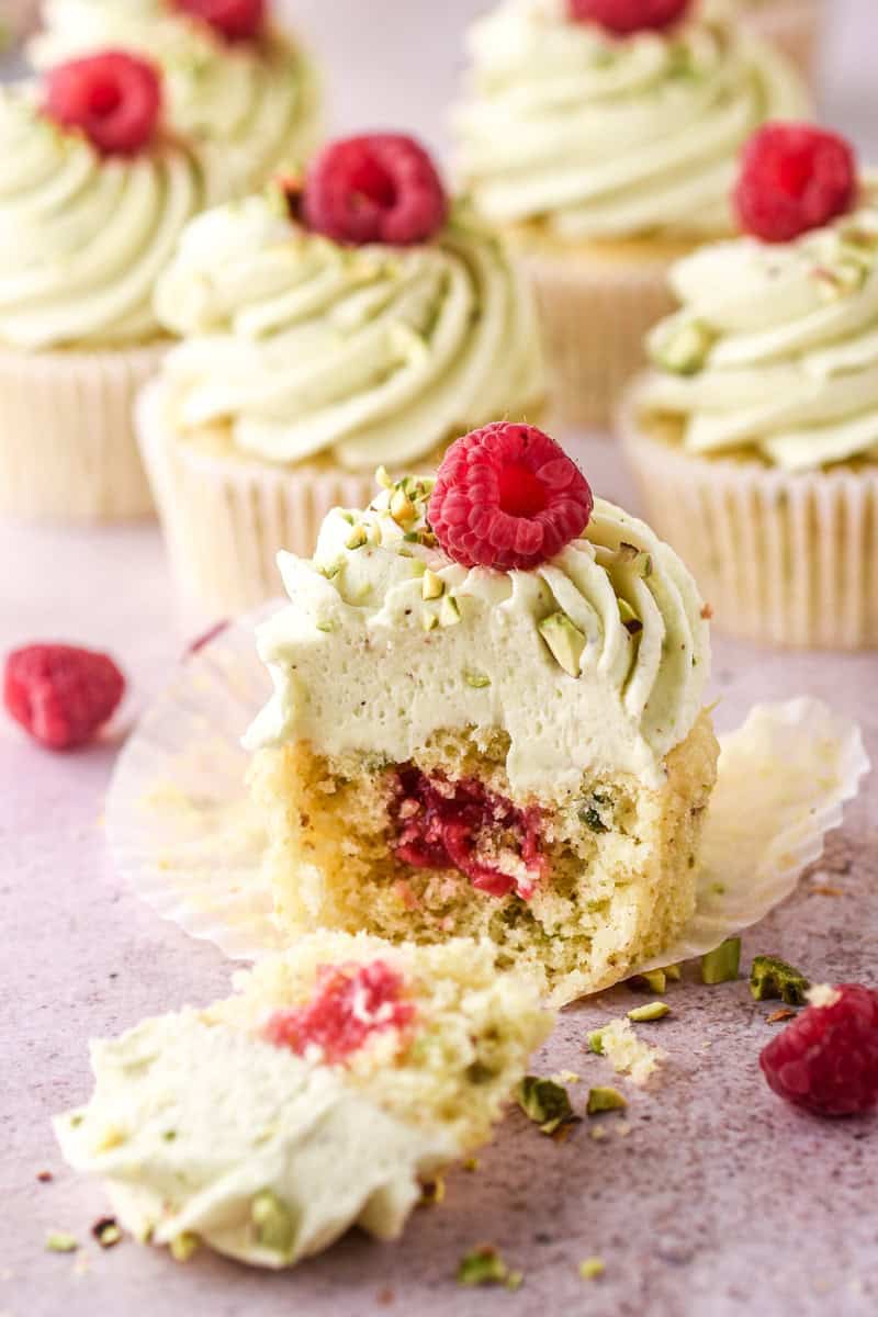 Pistachio Cupcake shown cut in half so that you can see the raspberry filling inside of the cupcake.