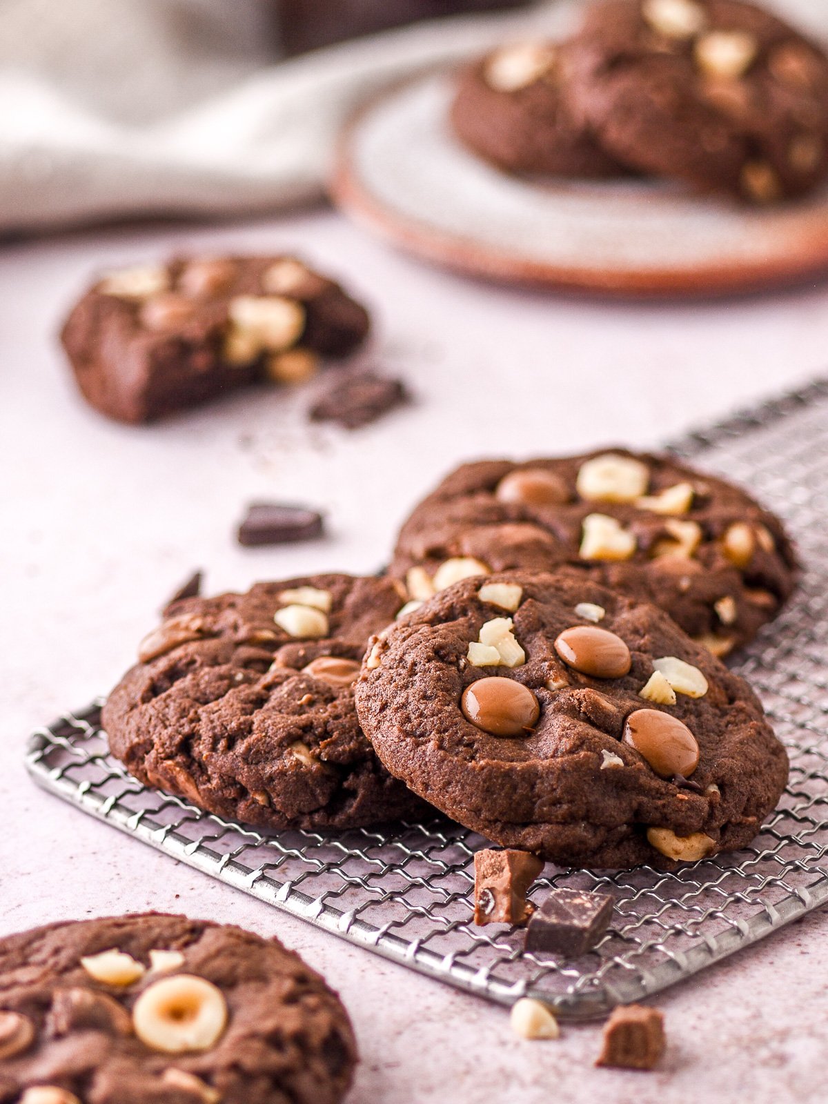 Hazelnut chocolate cookies shown on a wire cooling rack. There are cookies and chocolate chunks scattered around.