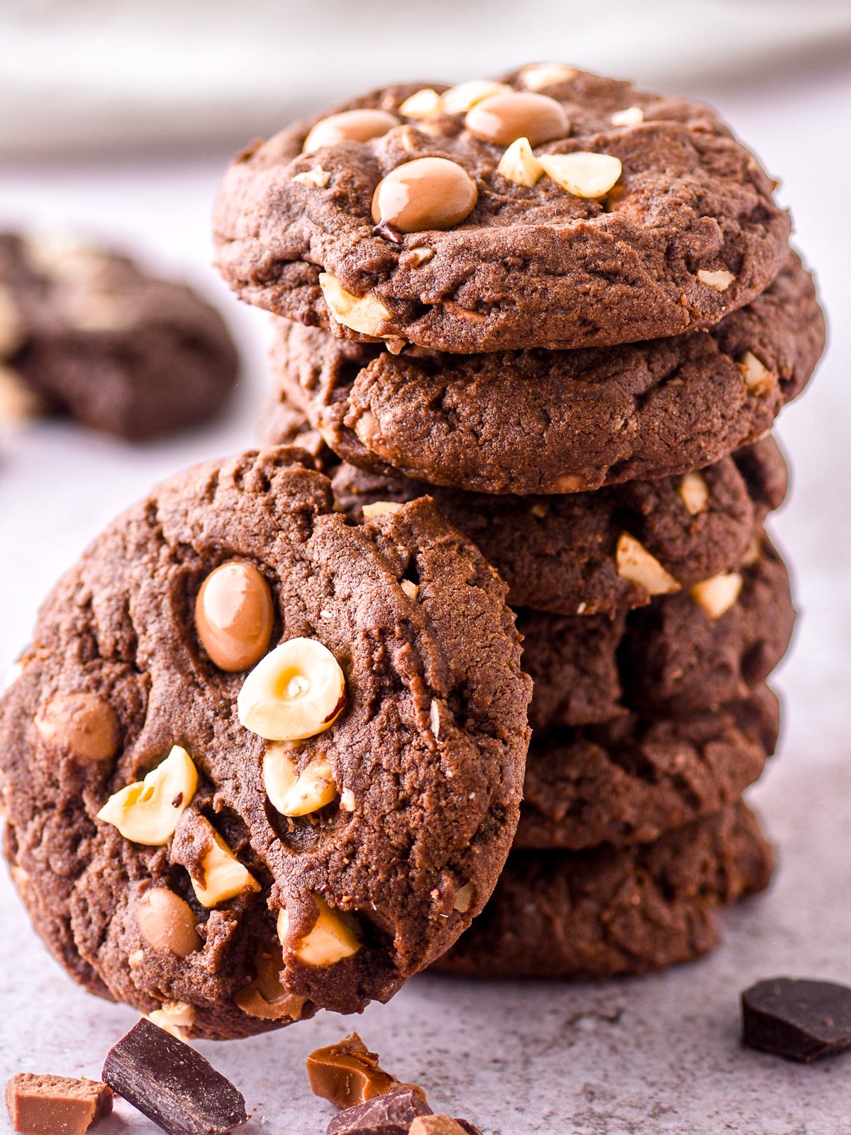 A pile of chocolate hazelnut cookie shown. There are dark and milk chocolate chunks in front of the cookies.
