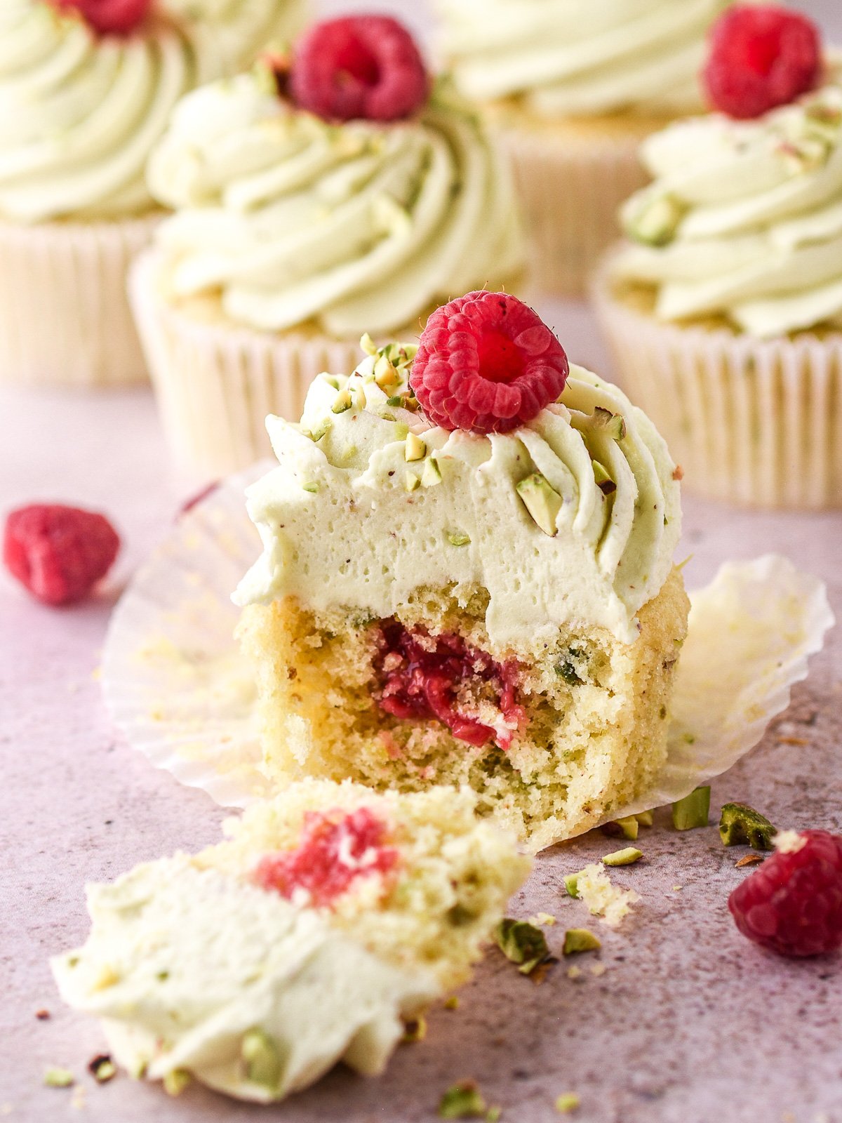 Pistachio cupcake shown sliced in half so that you can see the raspberry filling inside. 