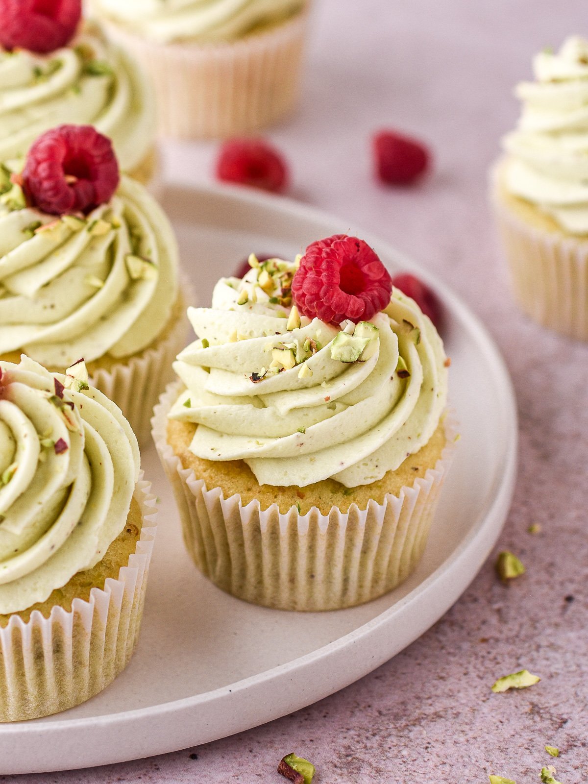 Pistachio cupcakes shown on a white plate on a kitchen counter. 