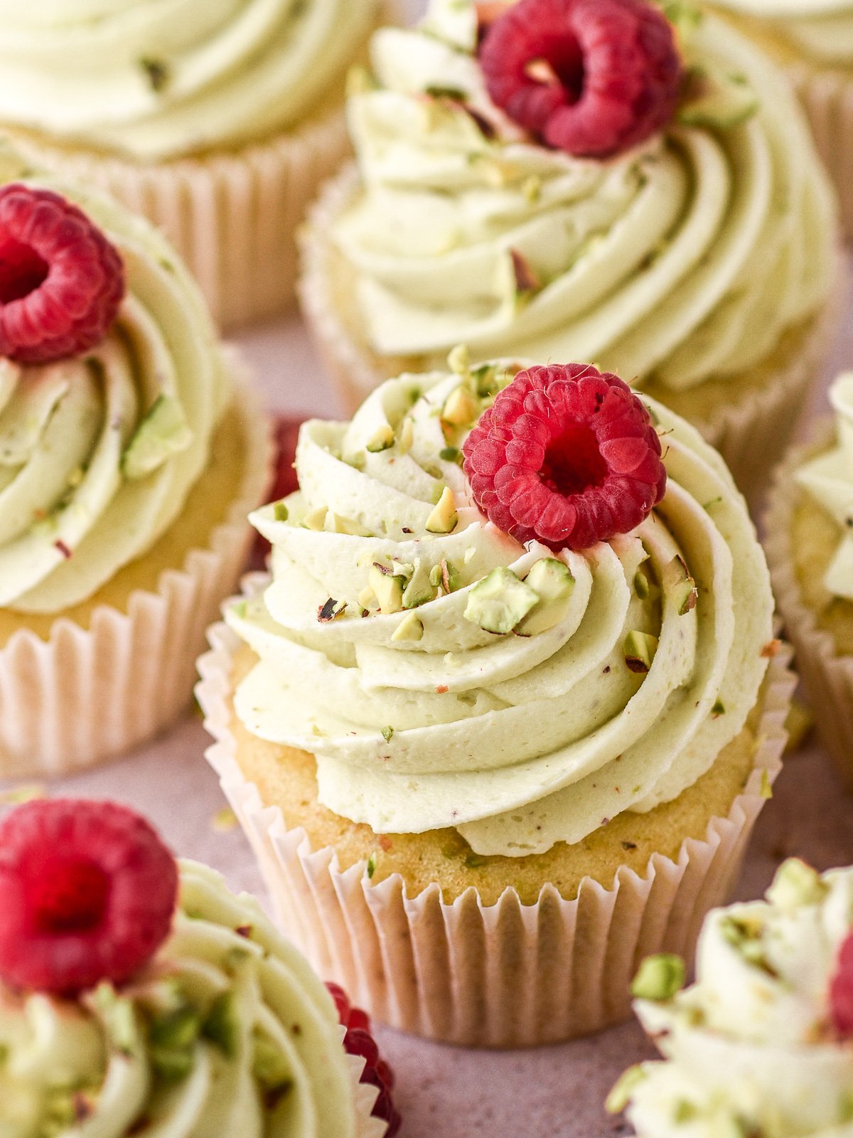 Pistachio cupcakes shown frosted and topped with fresh raspberries and chopped pistachios.