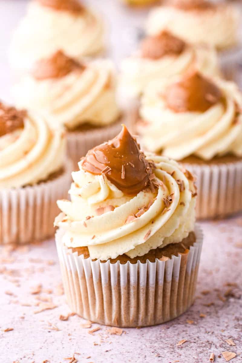 Banoffee Cupcakes shown up close so that you can see the layer of vanilla frosting topped with caramel and chocolate shavings.