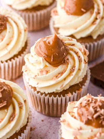 Banoffee cupcakes shown on a kitchen counter. You can see the big swirl of caramel on the cupcakes that has been decorated with chocolate shavings.