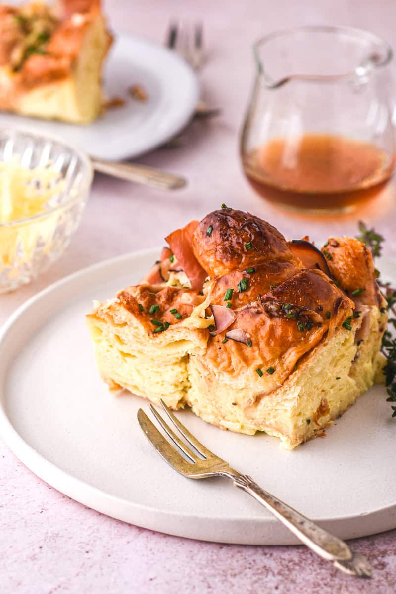 A slice of Croissant Ham and Cheese Bake shown on a white plate with a fork.