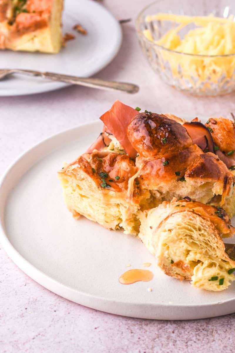 Croissant Ham and Cheese Bake slice shown on a white plate, drizzled with hot honey.