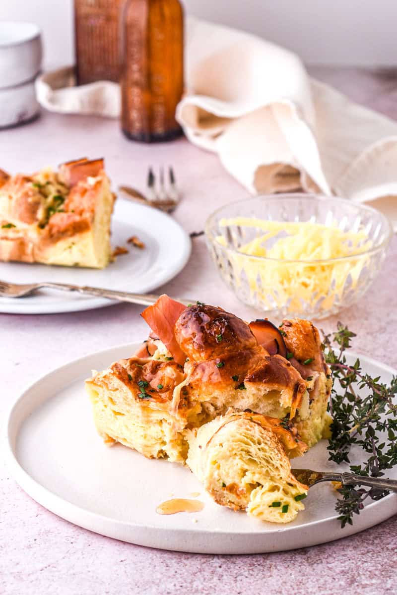 Croissant Ham and Cheese Bake slice shown on a white plate next to sprigs of fresh thyme.