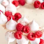 Mini meringues shown on a cake next to raspberries.
