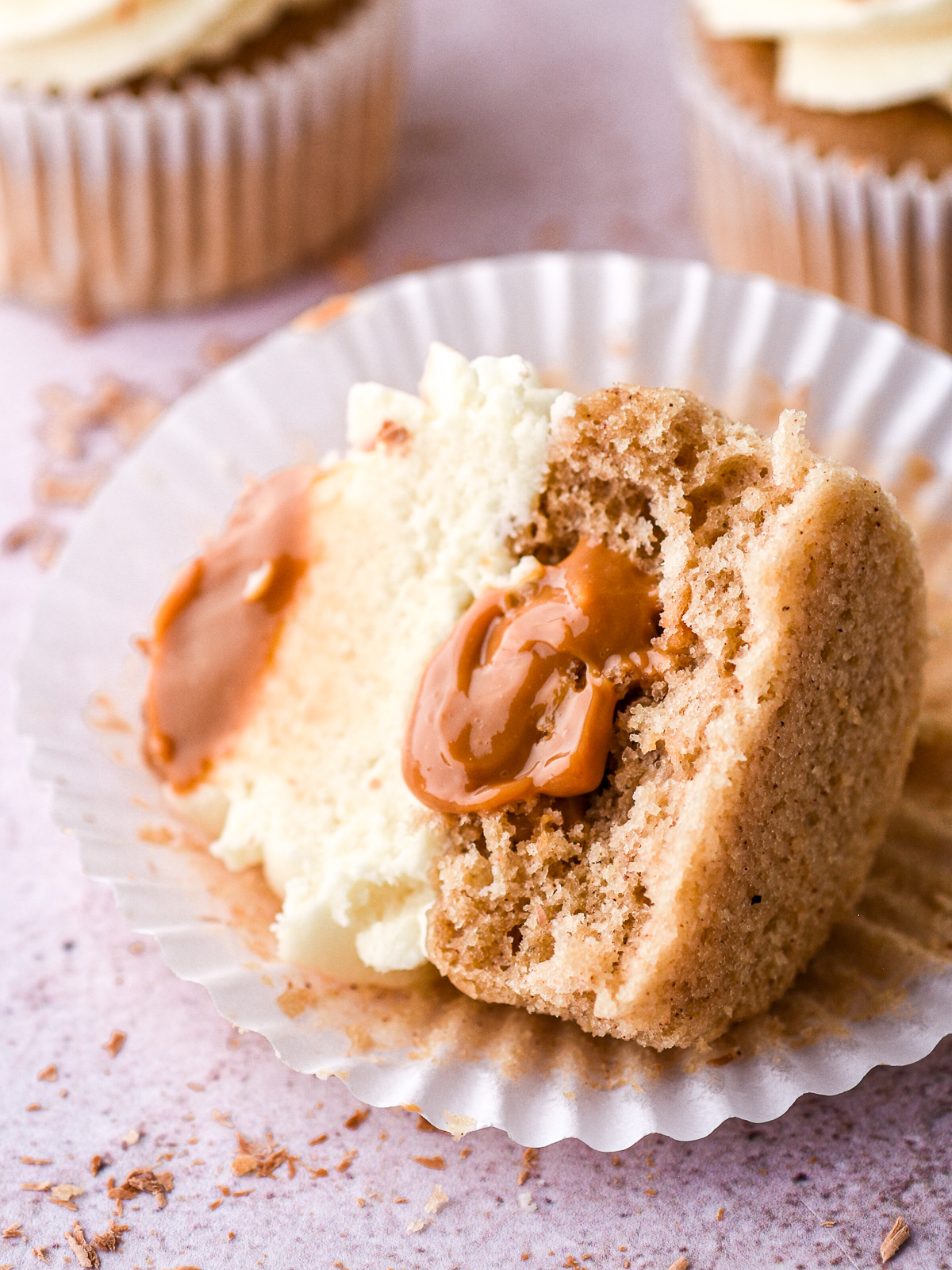 Banoffee Cupcake shown lying on its side in the cupcake paper, it is cut in half so that you can see the dulce de leche filling.