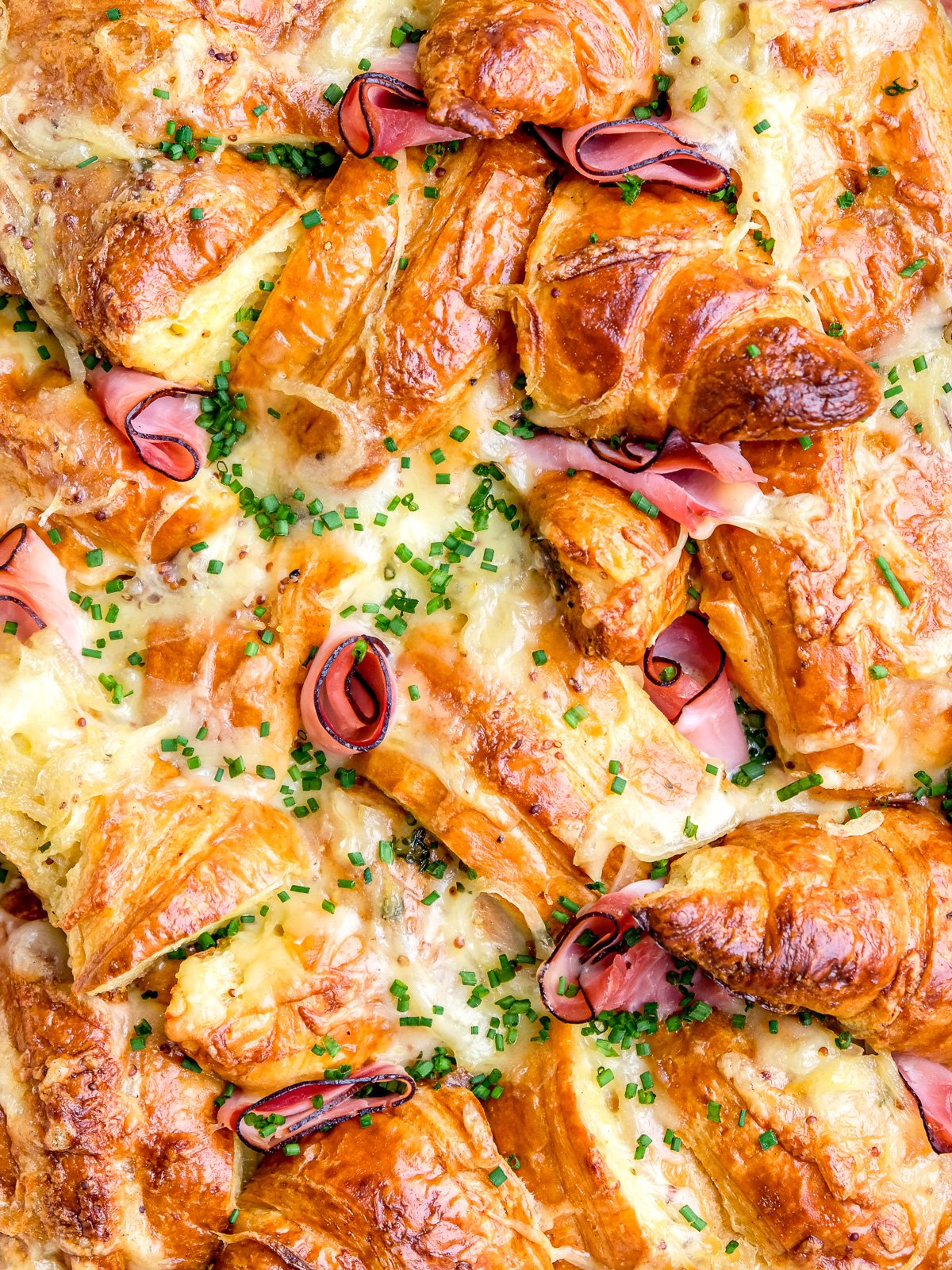 Image shows the croissant casserole up close, you can see the melted cheese and chopped chives clearly.