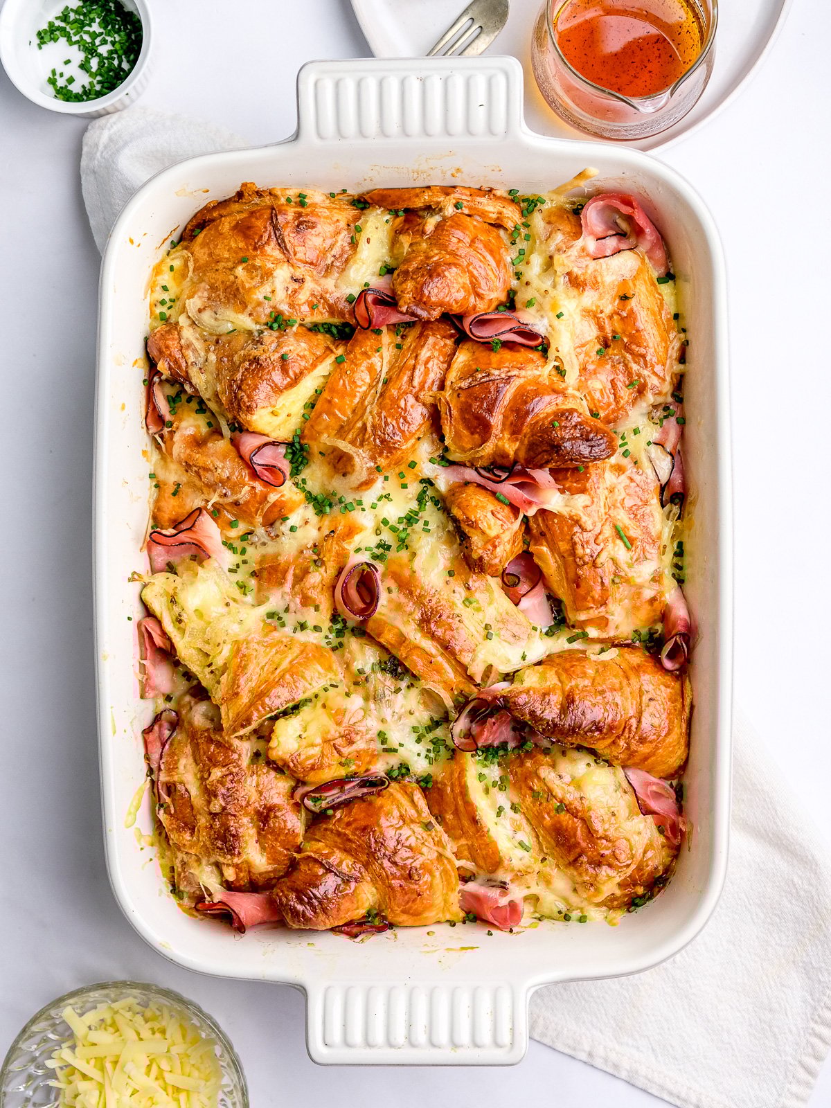 Ham and cheese croissant bake shown from above in a white casserole dish.