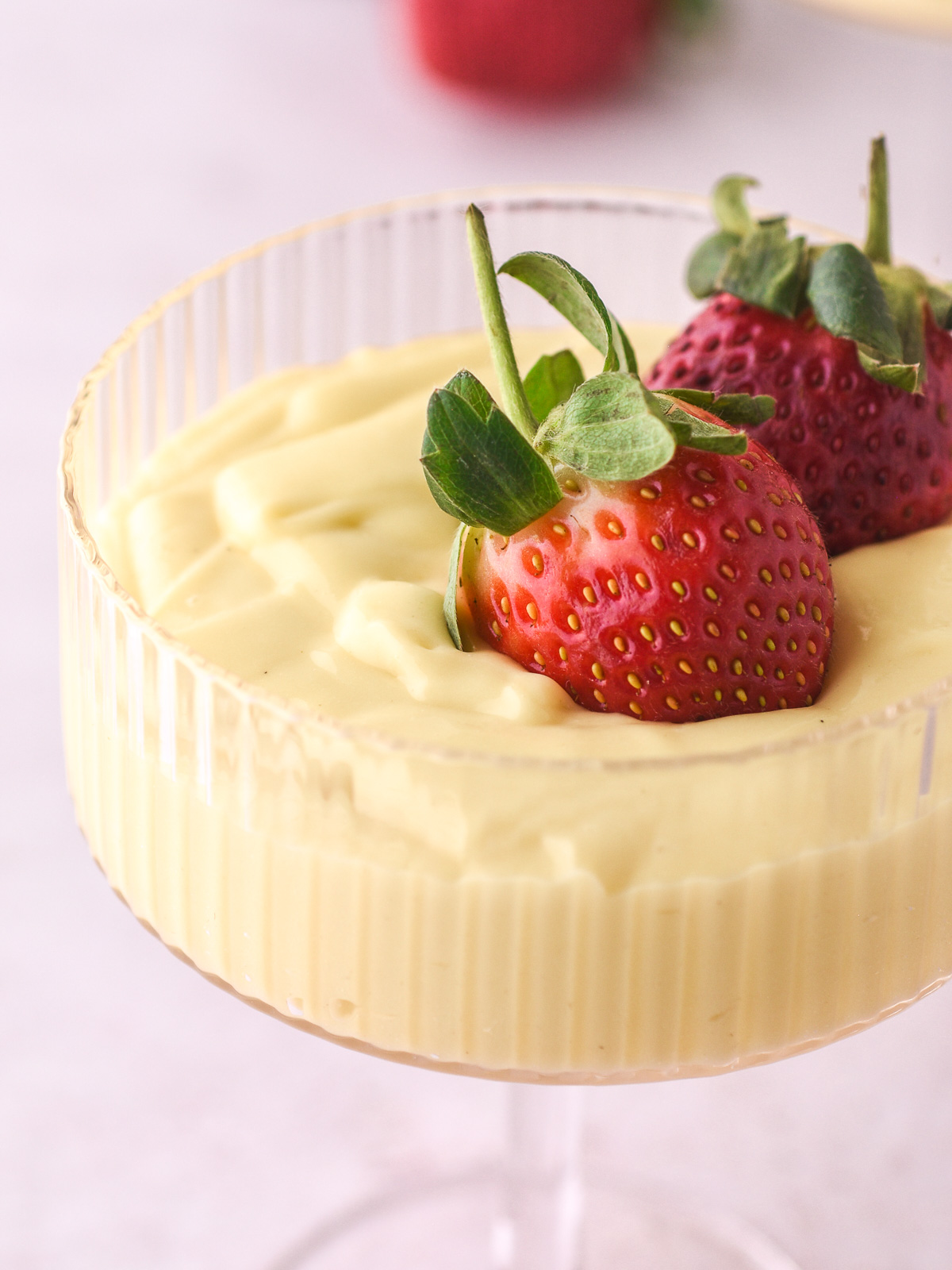 Vanilla Bean Custard shown in a dessert glass topped with fresh strawberries. The image is taken from up close and you can see the swirls of custard and the detail on the strawberries.
