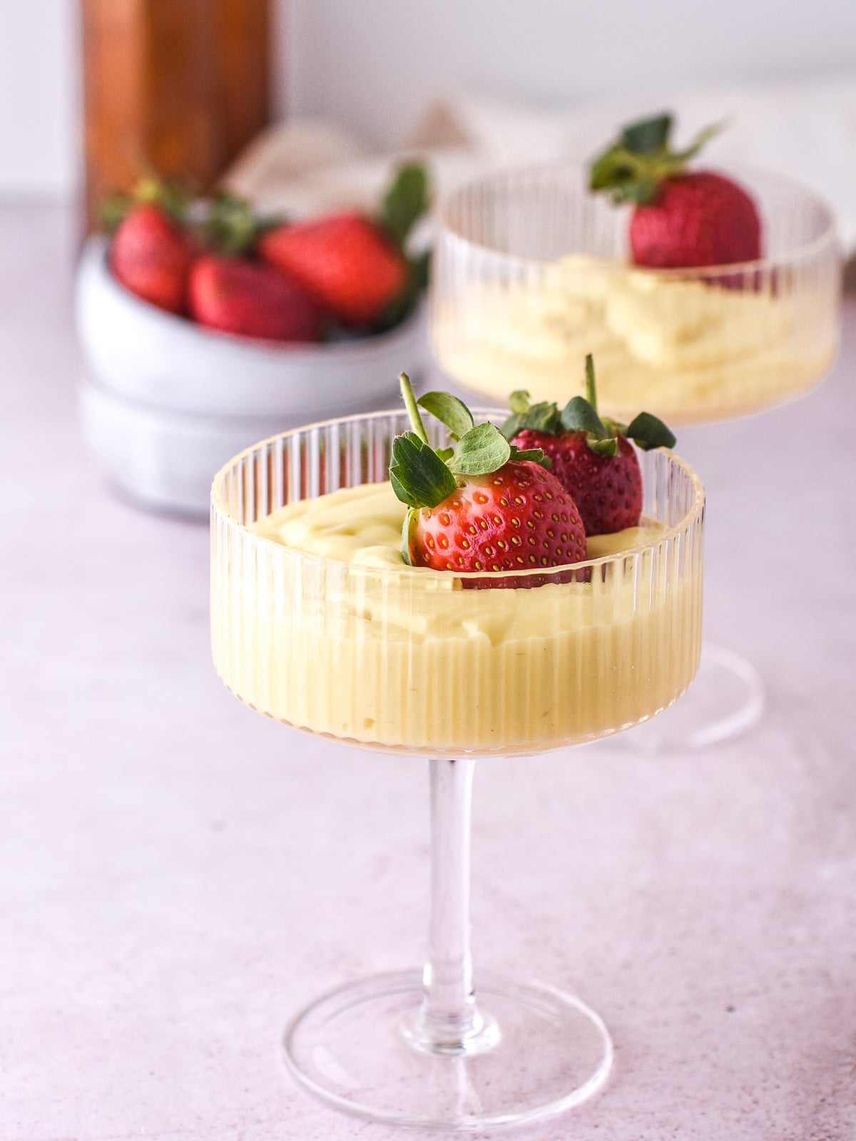 Vanilla Bean Custard shown in tall desert glasses topped with fresh strawberries.