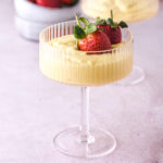 Image shows vanilla bean custard in a pretty glass with fresh strawberries.