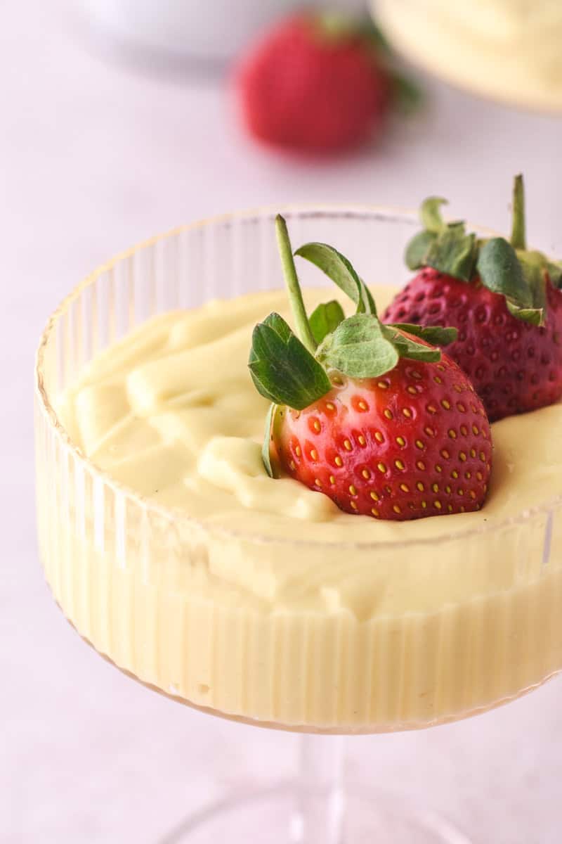 Vanilla Bean Custard shown in a dessert glass topped with fresh strawberries. The image is taken from up close and you can see the swirls of custard and the detail on the strawberries. 