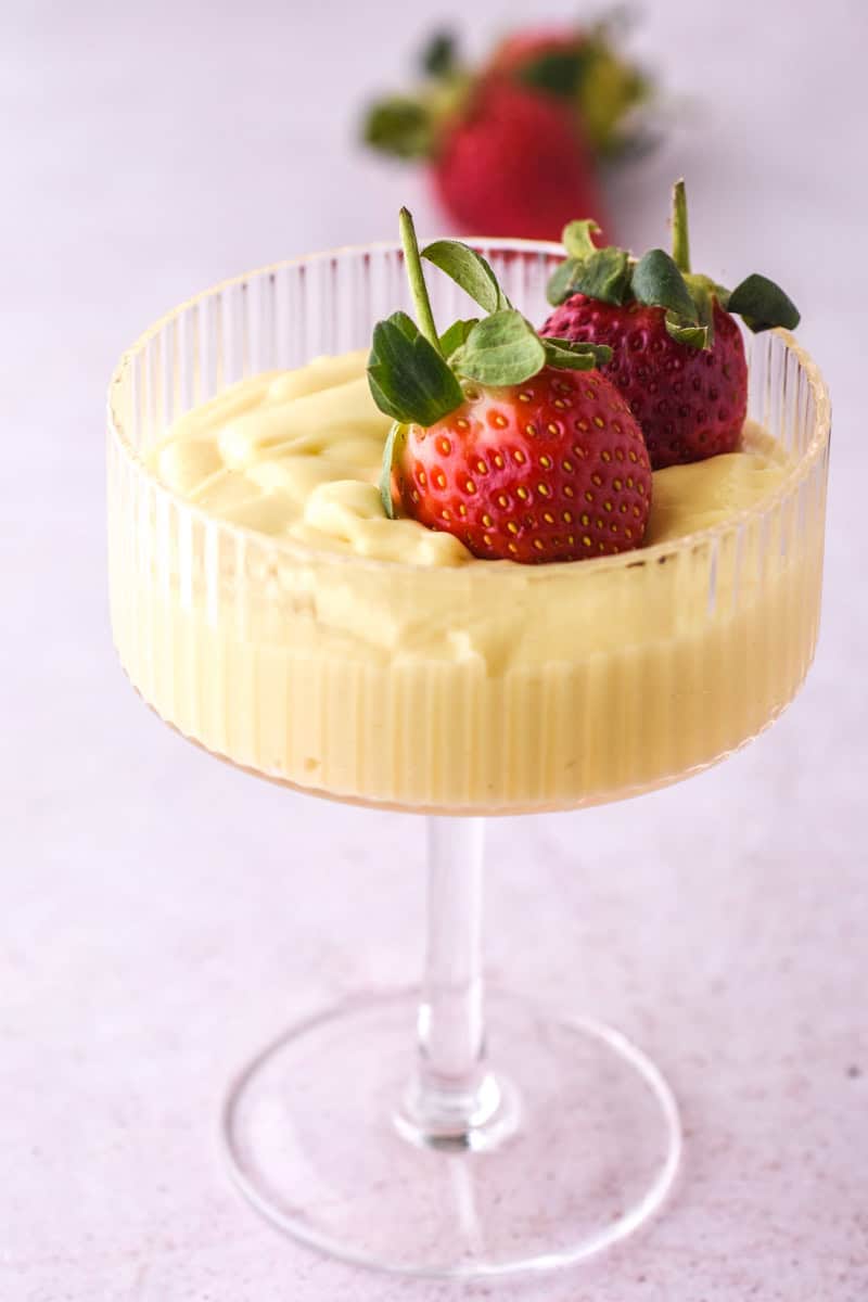 Vanilla Bean Custard shown in a dessert glass topped with fresh strawberries. 