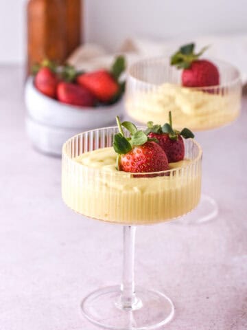 Vanilla Bean Custard shown in a tall stemmed dessert glass with fresh strawberries.