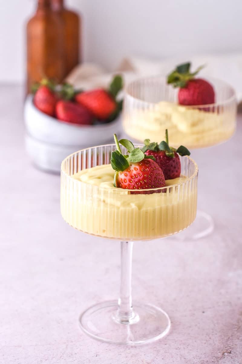 Vanilla Bean Custard shown in tall desert glasses topped with fresh strawberries.