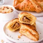 Bacon and Cheese Turnovers shown piled on a plate, one is cut open so that you can see the filling and the layers of flaky pastry.