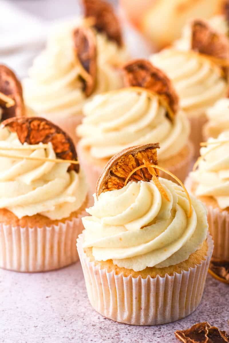 Image showing decorated cupcakes on a counter, you can see the orange rind and dried orange slice on top of the frosting.
