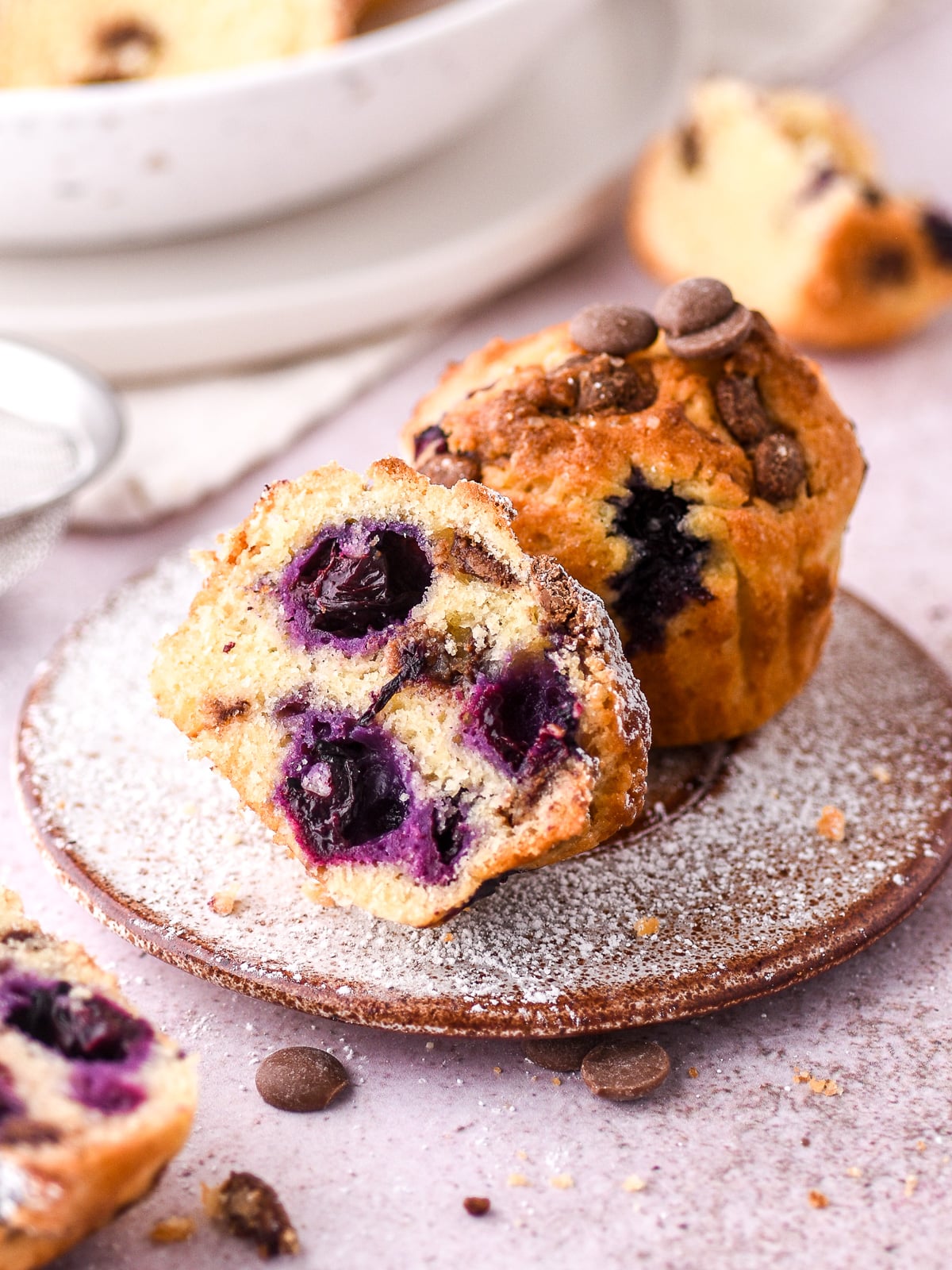 Image shows a blueberry and chocolate chip muffin cut in half. You can see the purple berries and chocolate chip studded throughout the muffin.