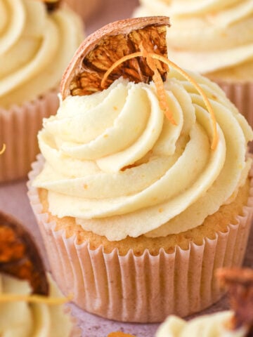 Orange cupcakes shown decorated and topped with dried slices of oranges.