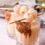 Image shows two lychee cocktails set on a kitchen counter, there is a bottle of tequila in the background.