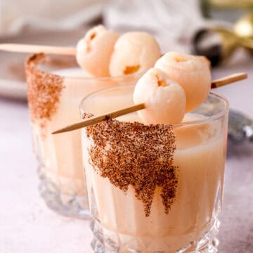 Image shows two lychee cocktails set on a kitchen counter, there is a bottle of tequila in the background.