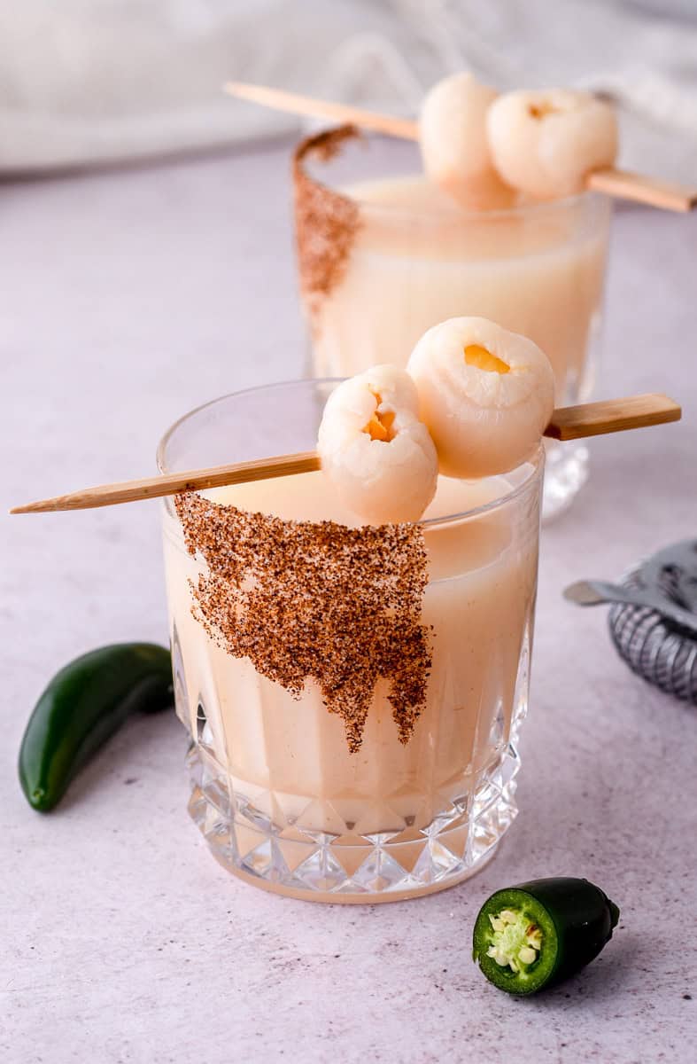 There are two glasses filled with the cocktail each one has a skewer with two litchis on it balanced over the rim of the glass. 