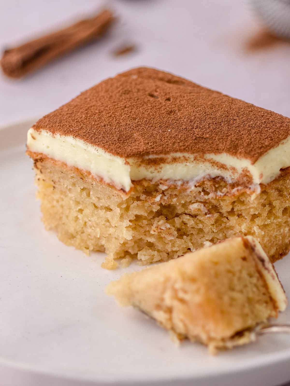 Image shows up close a slice of the melktert malva pudding. A fork has taken away a bite so that you can see the moist texture of the dessert.