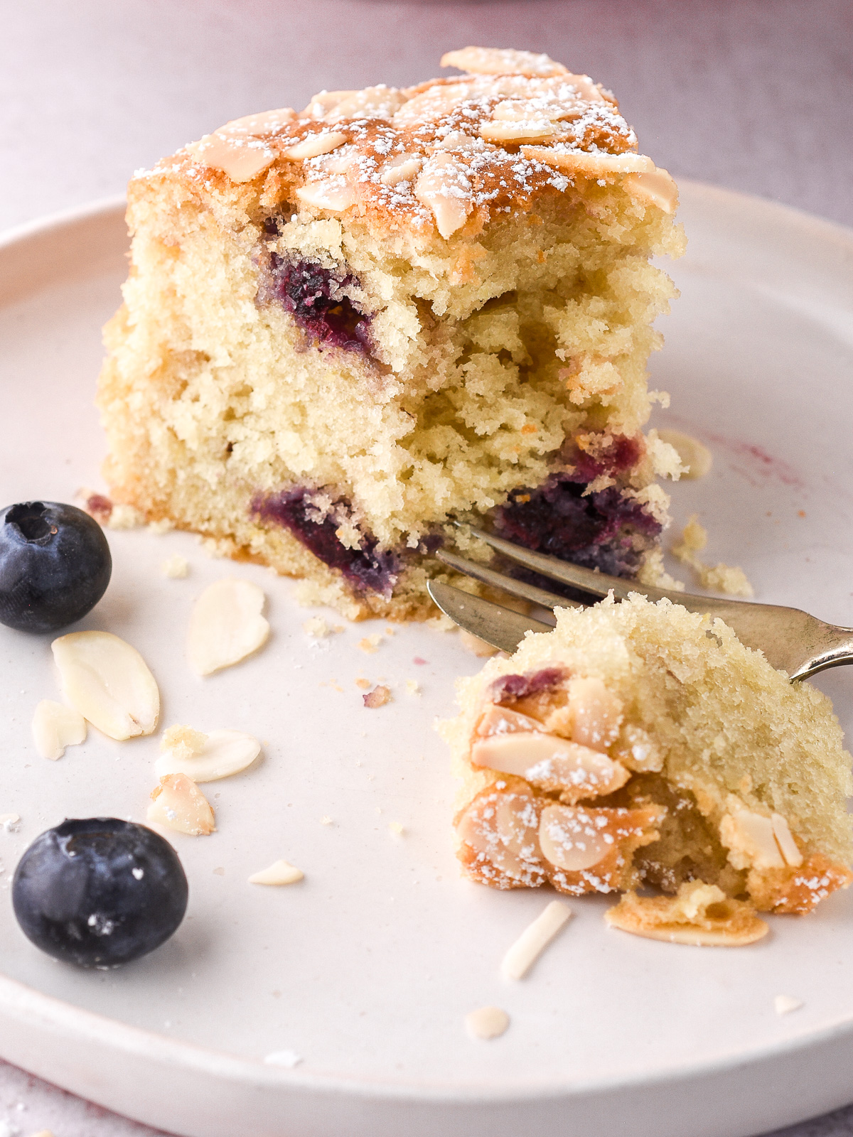 Image shows a slice of the lemon mixed berry cake half eaten. You can see the fluffy texture of the cake.