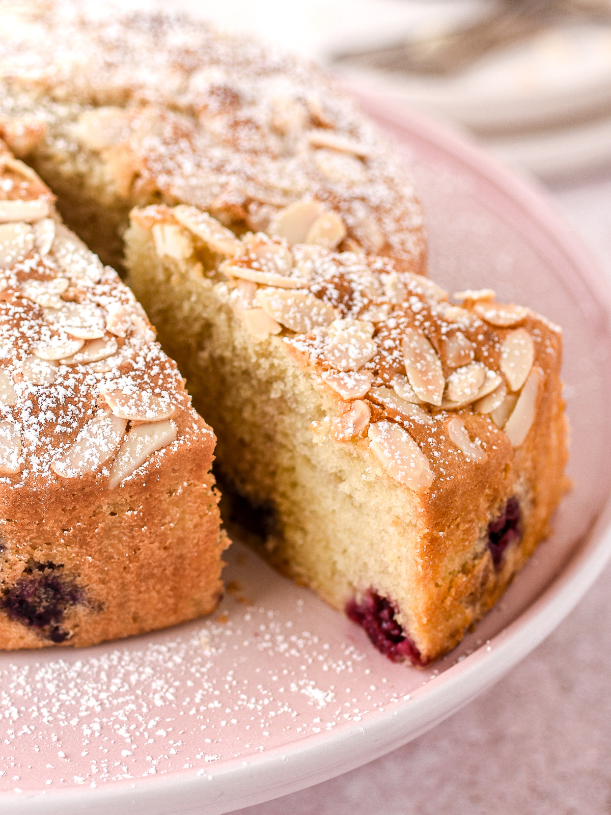 image shows the mixed berry cake from a close up view, one slice has been cut. You can see the crunchy almond topping in the berry cake.