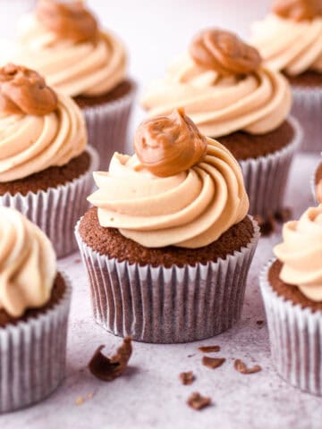 Dulce de leche cupcakes shown on a kitchen counter, each cupcake is decorated with a dollop of caramel on to top.