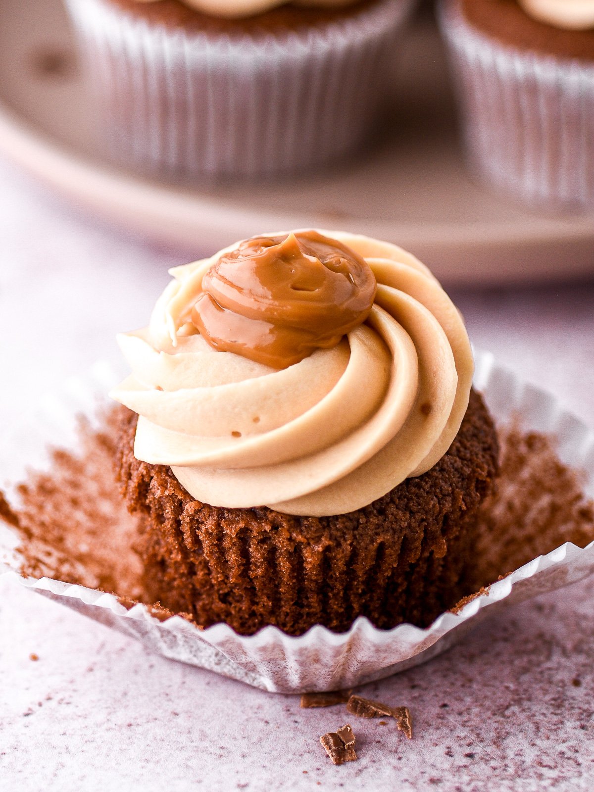 Chocolate caramel cupcake with dulce de leche frosting shown with the cupcake wrapper half off so that you can see the fluffy cupcake texture.