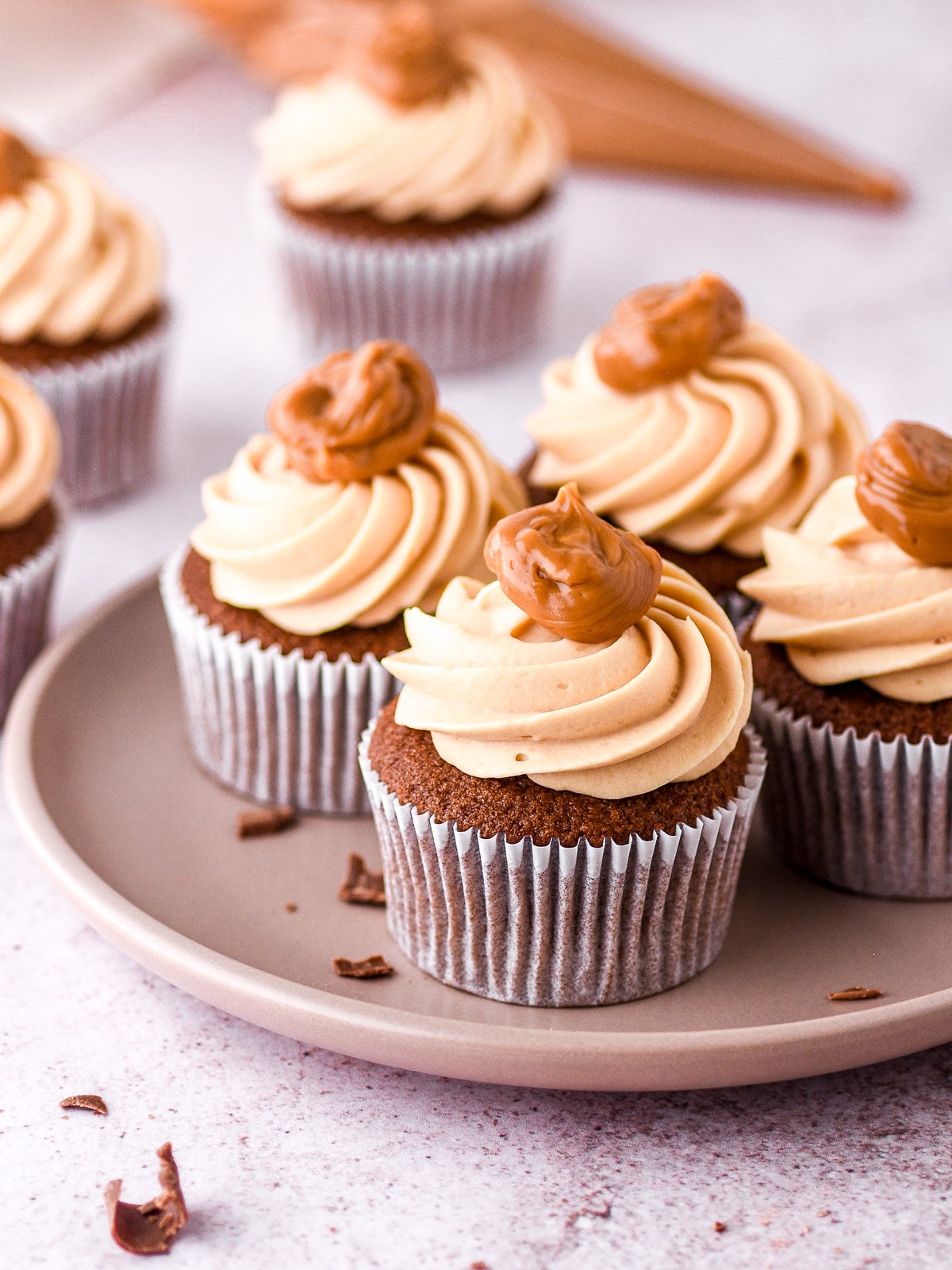 Chocolate dulce de leche cupcakes shown on a plate, there is a piping bag filled with dulce de leche in the background.