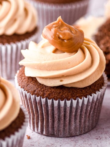 Dulce de leche chocolate cupcake shown on a kitchen counter with more cupcakes in the background.