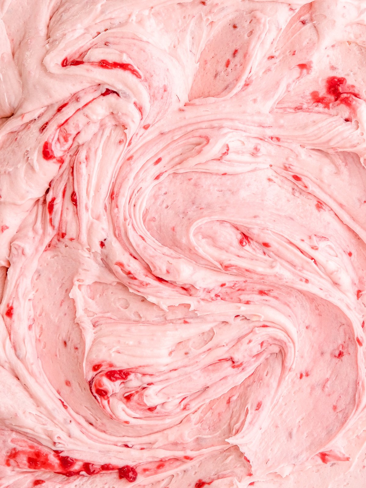 Image showing the raspberry cream cheese frosting up close, you can see the silky texture and the raspberry seeds.
