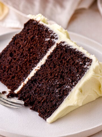A slice of chocolate cake with cream cheese frosting shown on a white plate.