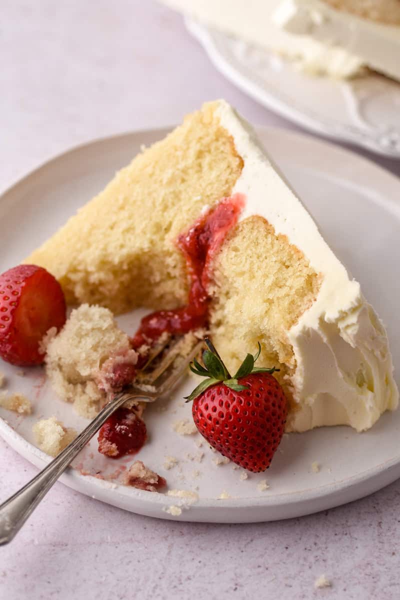 Image showing a half eaten piece of cake, you can see the fluffy texture of the vanilla sponge. 