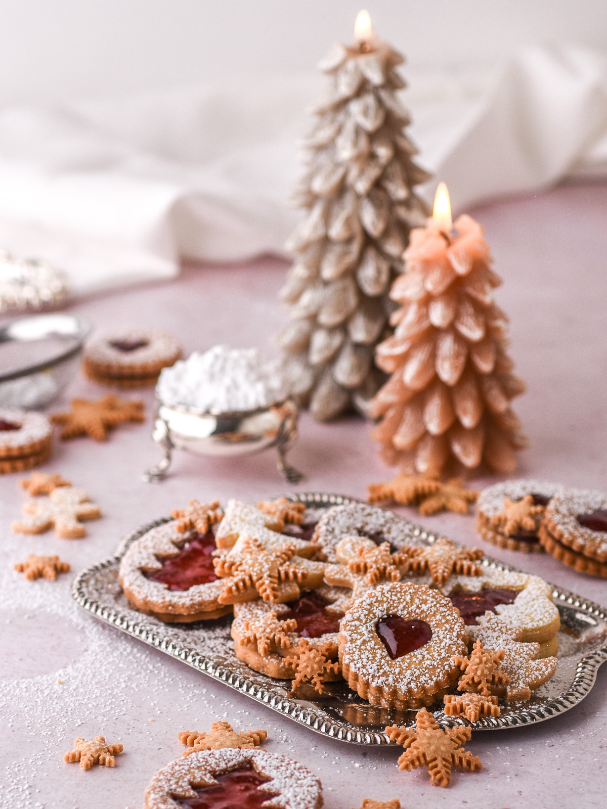 Christmas Butter Cookies shown on a tray and others on a kitchen counter. There are lit Christmas tree candles in the background.