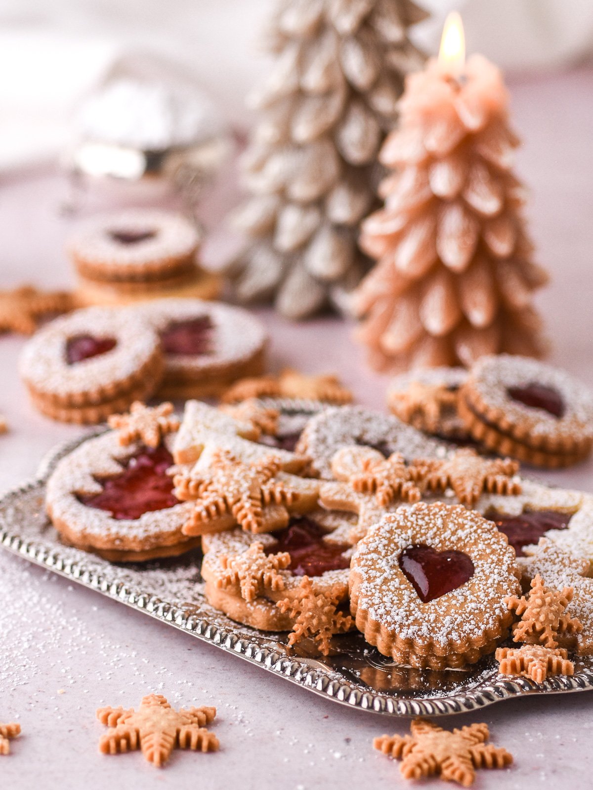 Christmas Butter Cookies of different shapes shown on a silver tray, there are Christmas tree candles in the background.