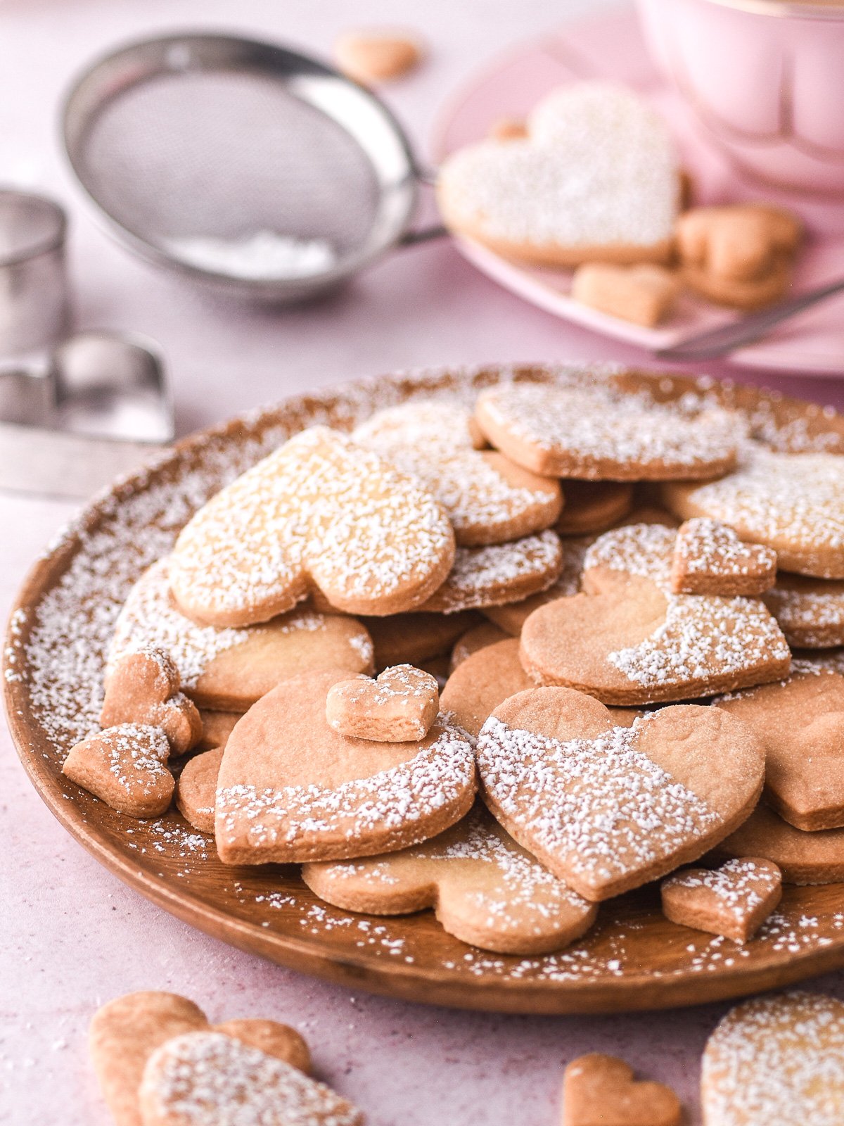 Image shows heart shape biscuits dusted with icing sugar on a wooden plate.