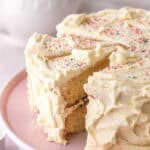 Vanilla buttercream cake shown on a pink cake stand with some slices cut.