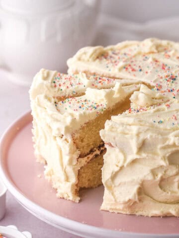 Vanilla buttercream cake shown on a pink cake stand with some slices cut.